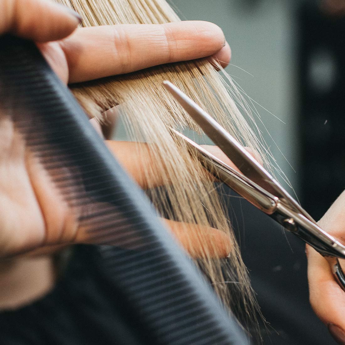 A person cutting their hair with scissors and comb.