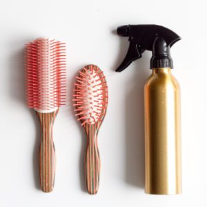 A bottle of hair spray, two brushes and a spray bottle.