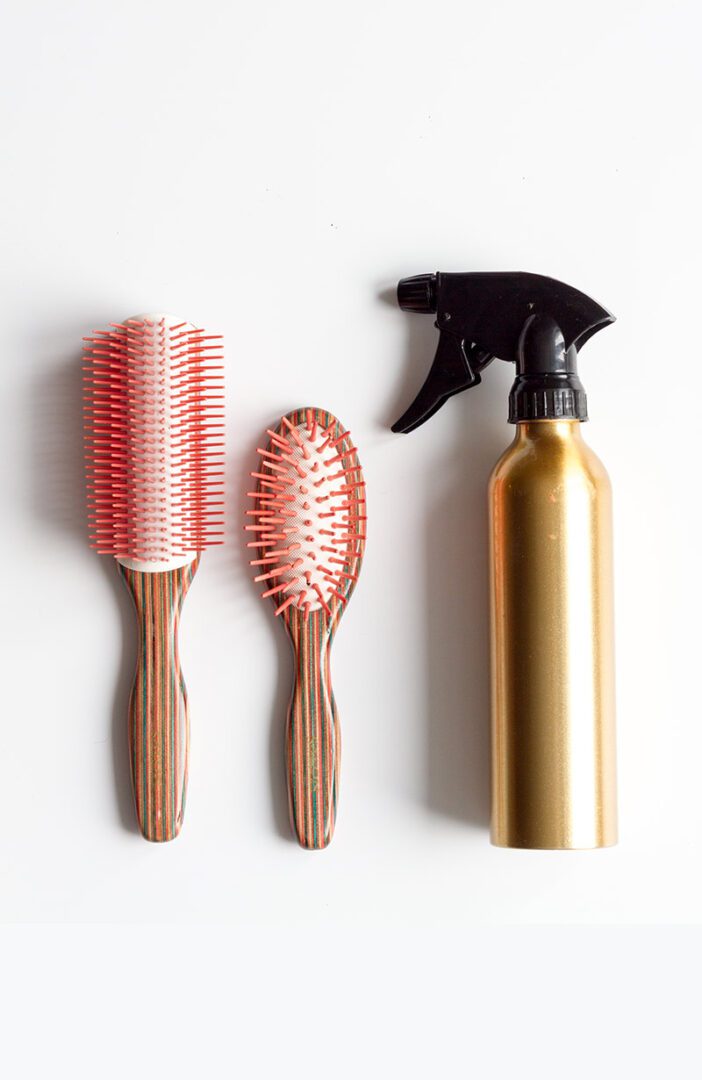 A bottle of hair spray, two brushes and a spray bottle.