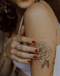 A woman with red nails and a flower tattoo on her arm.