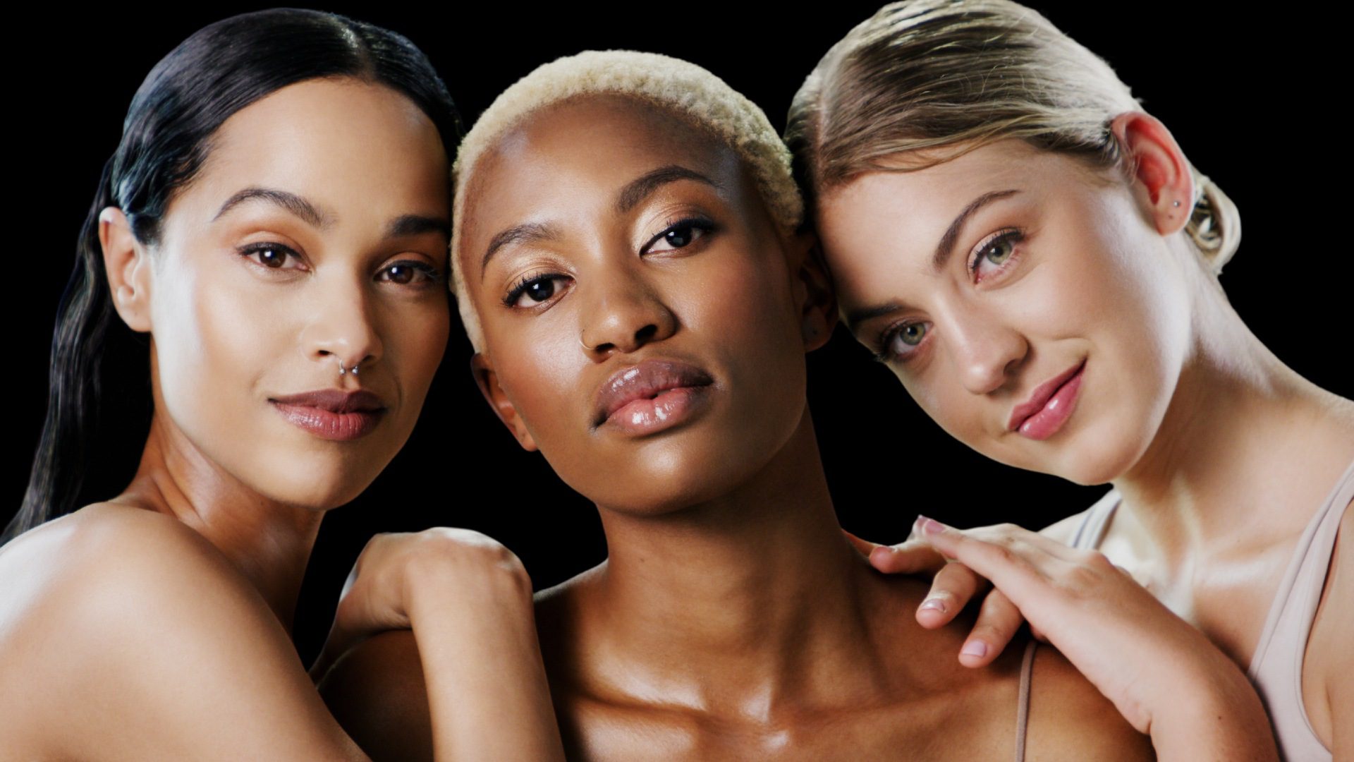 Three women posing for a picture in front of black background.